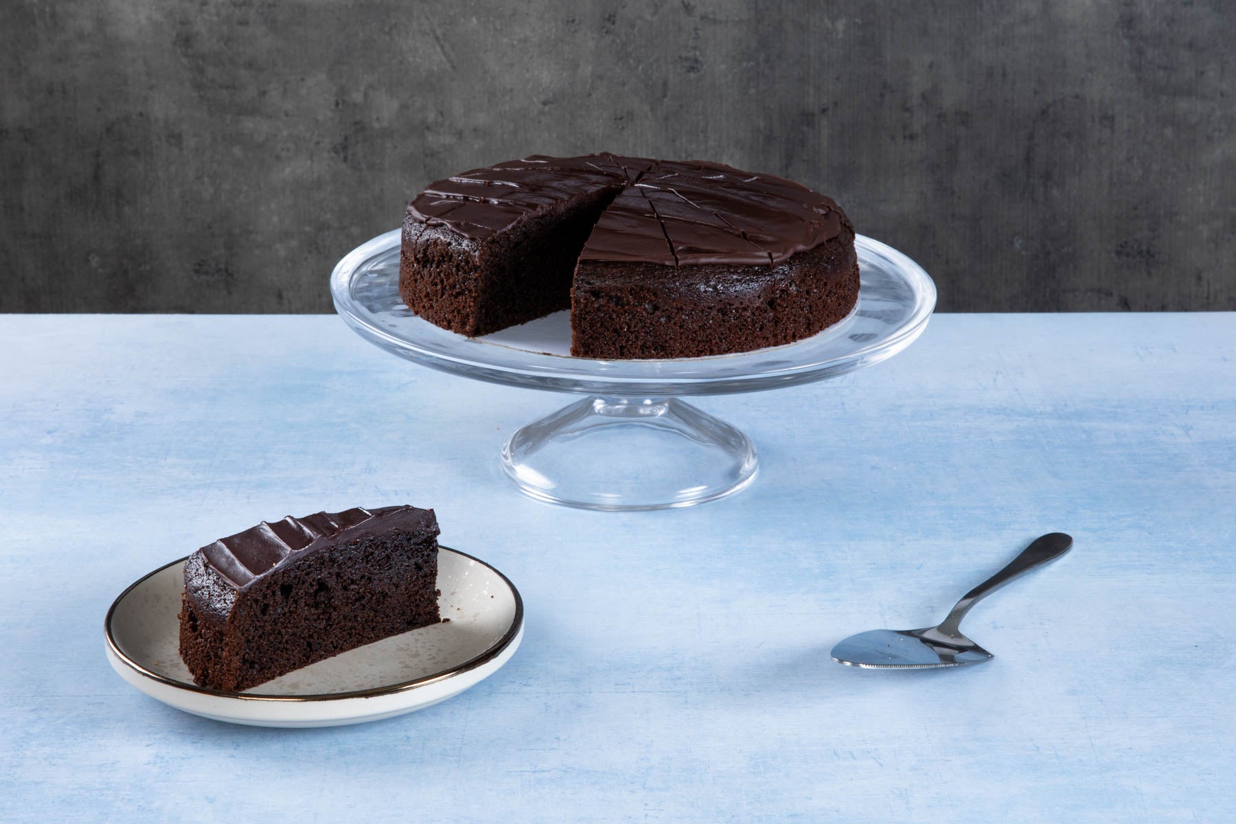 LHMC008-250.jpg Chocolate cake with creamy frosting and chocolate topping on a wooden board.